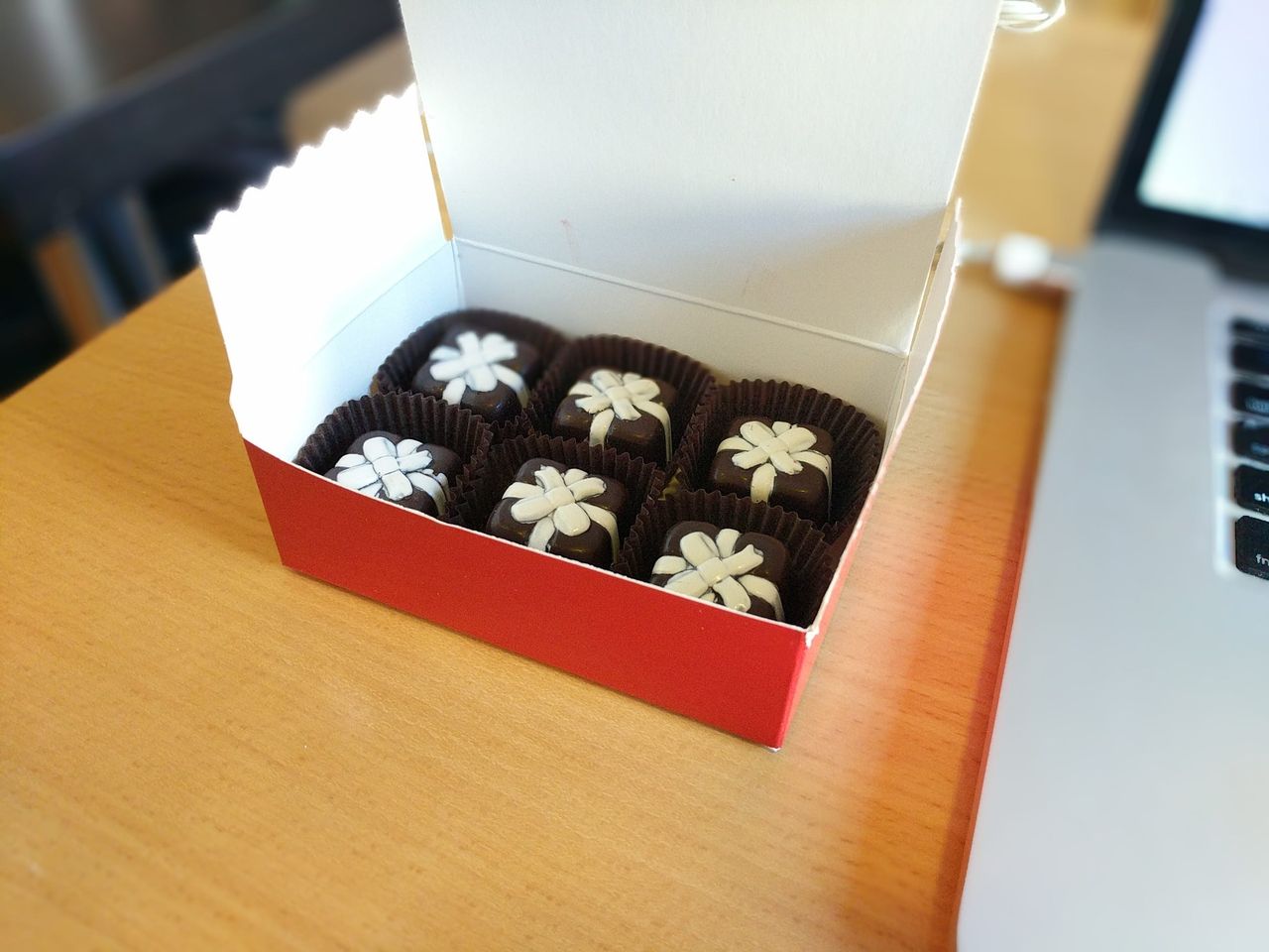 An open box of six chocolate eggnog truffles, each topped with a white icing flower