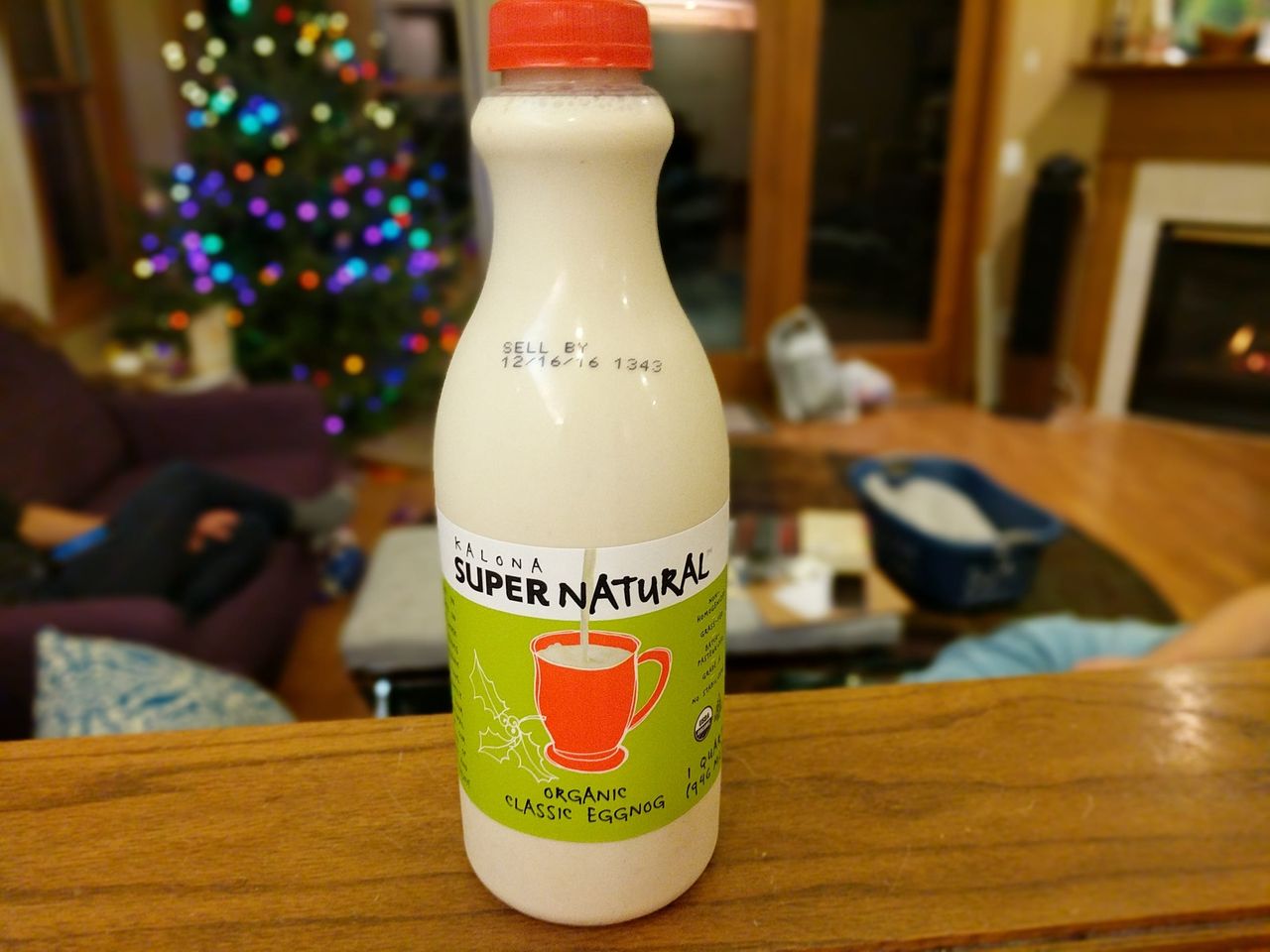 A bottle of Kalona SuperNatural Organic Classic Eggnog in front of a lit Christmas tree