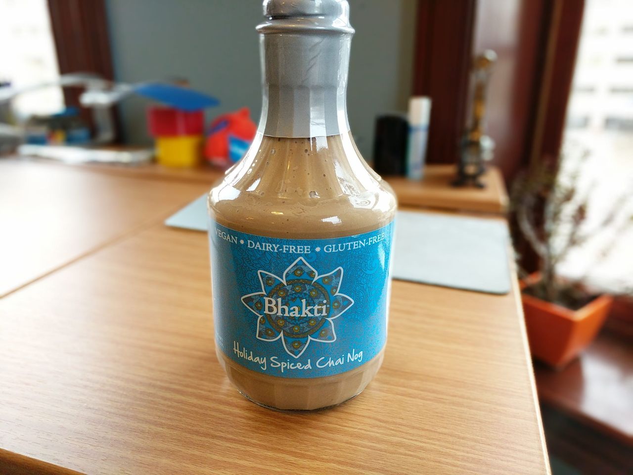 A full bottle of Bhakti Holiday Spiced Chai Nog on a wooden desk